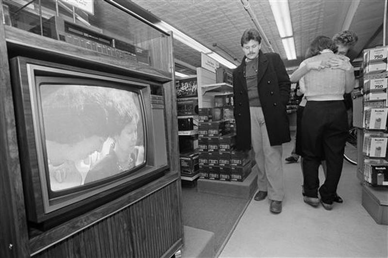 FILE - In this Friday, Feb. 1, 1986 file photo, customer David Kimball of Manchester, N.H. reacts as store employees Lynne Beck of Salisbury, N.H. and Lisa Olson, far right, of Manchester, N.H., embrace each other as they watch the Houston memorial service for the astronauts who died in the space shuttle Challenger explosion on a television in a store in Concord, N.H. Pictured on the television screen are family members of one of the astronauts. (AP Photo/Charles Krupa)