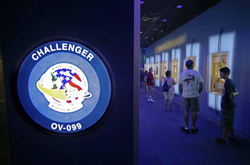In this Tuesday, July 21, 2015 photo, visitors look over display cases at the "Forever Remembered" exhibit and memorial for the astronauts that perished on the Columbia and Challenger space shuttles, at the Kennedy Space Center Visitor Complex in Cape Canaveral, Fla. (AP Photo/John Raoux)
